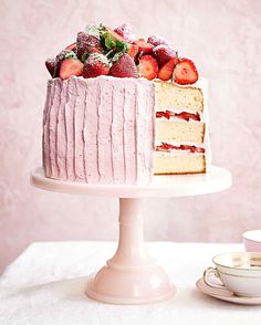 a white cake with strawberries on top sitting next to a cup and saucer