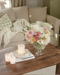 a coffee table with flowers and candles on it in front of a couch that has pillows