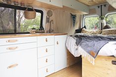 the interior of a camper with white cabinets and wood flooring, including a bed