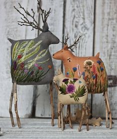 two deer made out of fabric sitting next to each other on a wooden surface with flowers and grass