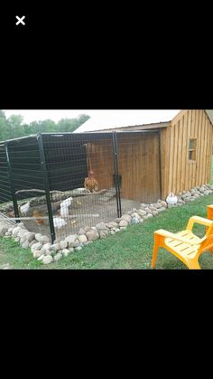 a chicken coop with two chickens in it and an orange plastic chair next to it