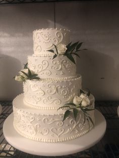 a three tiered white wedding cake with flowers on the top and bottom, sitting on a wire rack