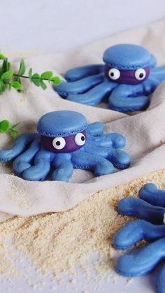 three blue octopus figurines sitting on top of a white cloth covered in sand