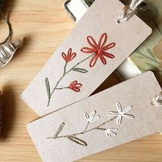 two tags with embroidered flowers on them are sitting on a table next to other items