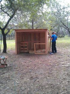 a man standing next to a wooden shed in the middle of a field with trees