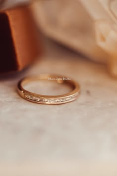 a gold wedding band sitting on top of a white table next to a brown ribbon