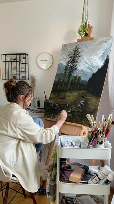 a woman sitting in front of an easel painting