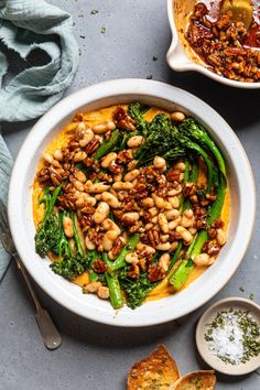 a white bowl filled with beans and broccoli next to other dishes on a table