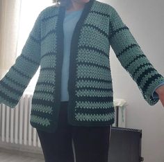 a woman standing in front of a window wearing a green and black crocheted cardigan