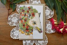 a card with an image of a horse surrounded by flowers and leaves on a doily