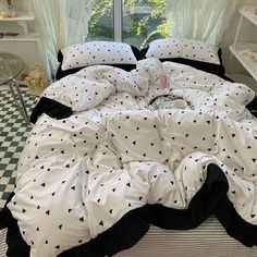 an unmade bed with black and white comforter in a bedroom next to a window