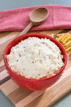 a red bowl filled with mashed potatoes on top of a wooden cutting board next to french fries