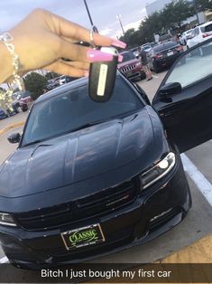 a person holding a car key in front of a black car with other cars behind it