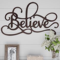 a metal sign that says believe next to a vase with flowers in it and two pictures on the wall