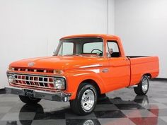 an orange pick up truck is parked in a room with black and white checkered flooring