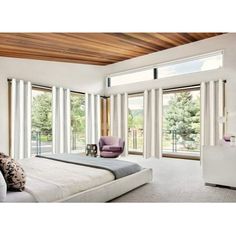 a bedroom with white walls and wood ceilinging, large bed in front of sliding glass doors