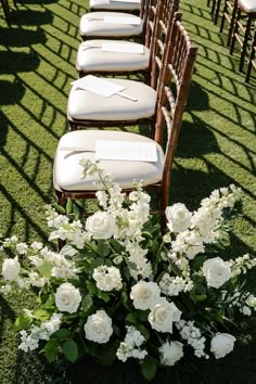 rows of chairs lined up with white flowers and greenery on the grass in front of them