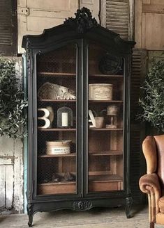 an old fashioned china cabinet with glass doors and shelves in the corner, next to a chair