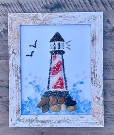 a picture frame with rocks in front of it and a lighthouse painted on the side