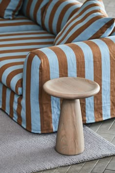 a wooden stool sitting on top of a rug in front of a striped couch and chair