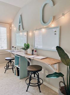 a room with two desks and three stools in front of the wall that has letters on it