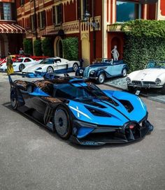 a blue and black sports car parked in front of a building with other cars behind it