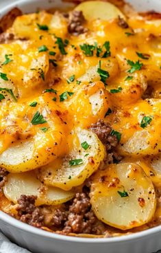 a white bowl filled with potatoes and meat covered in cheese on top of a table