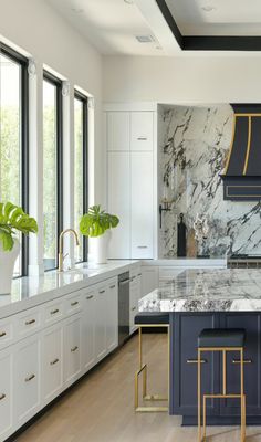 a large kitchen with marble counter tops and white cabinets, along with two stools