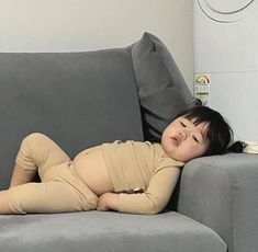 a baby laying on top of a gray couch