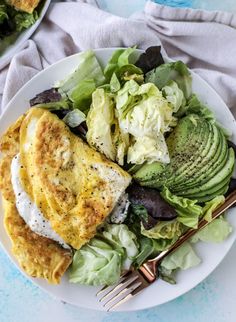 a white plate topped with an omelet next to a green salad and fork