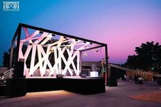 the stage is set up for an outdoor concert at dusk with people standing around it