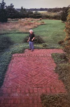 an old man standing on a brick path in the middle of a field with grass