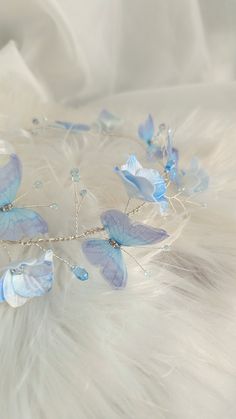 a tiara with blue butterflies and pearls on it's headband, sitting on a feathery surface