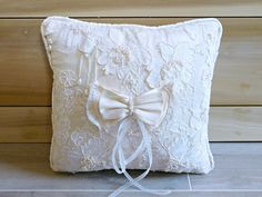 a white pillow with a bow on the front and lace trim around the back, sitting on a wooden floor