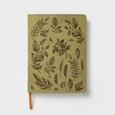 a green notebook with leaves drawn on the front and side, sitting on top of a white surface