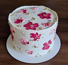 a white cake with pink and gold flowers on it sitting on top of a wooden table