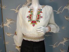 Stunning vintage hand embroidered peasant blouse dating from 1970s. Made from a semi-sheer Diolen polyester fabric, it has a beautiful embroidered floral design in primary colours on the front and sleeves. It has wide puff sleeves, smocking at the neckline, waist and cuffs, and blanket stitched rolled hems. It fastens at the side with silver poppers. Labelled size 38, would fit a UK 8/ 10. Measures a loose fitting 40" bust. Waist 24" stretching to 28". Length 18.5" from shoulder to hem. In excel Traditional Spring Blouse With Machine Embroidery, Spring Fitted Blouse With Embroidered Border, Fitted Blouse With Embroidered Border For Spring, Traditional Spring Peasant Top With Embroidered Neckline, Spring Peasant Top With Embroidered Border, Fitted Traditional Embroidered Peasant Top, Spring Embroidered Border Peasant Top, Spring Embroidered Peasant Top, Traditional Blouse With Embroidered Border For Spring