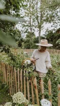 a woman in a straw hat is tending to her garden with white flowers and greenery