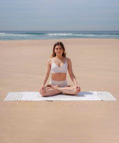 a woman sitting in the middle of a yoga pose on a towel at the beach