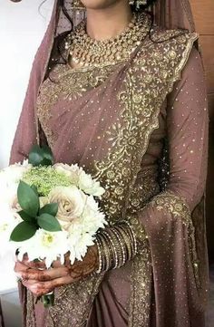 a woman in a bridal gown holding a bouquet of white flowers and greenery