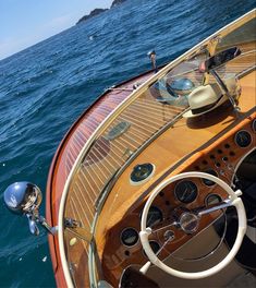 the steering wheel and dashboard of a wooden boat in the open water with an island in the background