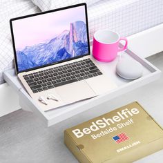 an open laptop computer sitting on top of a white desk next to a pink mug