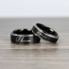 two black wedding rings with the word leno engraved on them sitting on a wooden surface