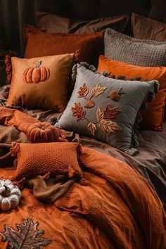 a bed covered in lots of pillows and blankets with pumpkins on top of it