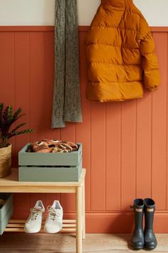 an orange coat hangs on the wall next to a wooden table with shoes in it