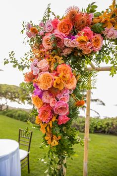 an arrangement of flowers and greenery on a wooden pole at a wedding reception in the grass