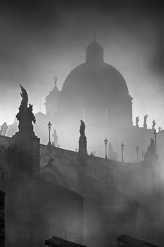 black and white photograph of an old building with statues on it's roof in the fog