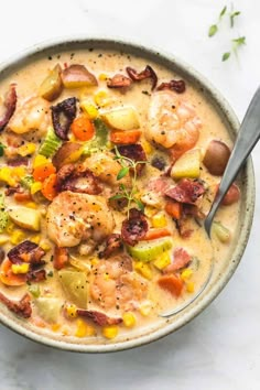 a bowl filled with shrimp, potatoes and carrots on top of a white table