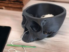 a black skull shaped cup sitting on top of a wooden table next to a laptop computer