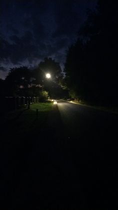 a street light shining on the side of a road at night with trees in the background